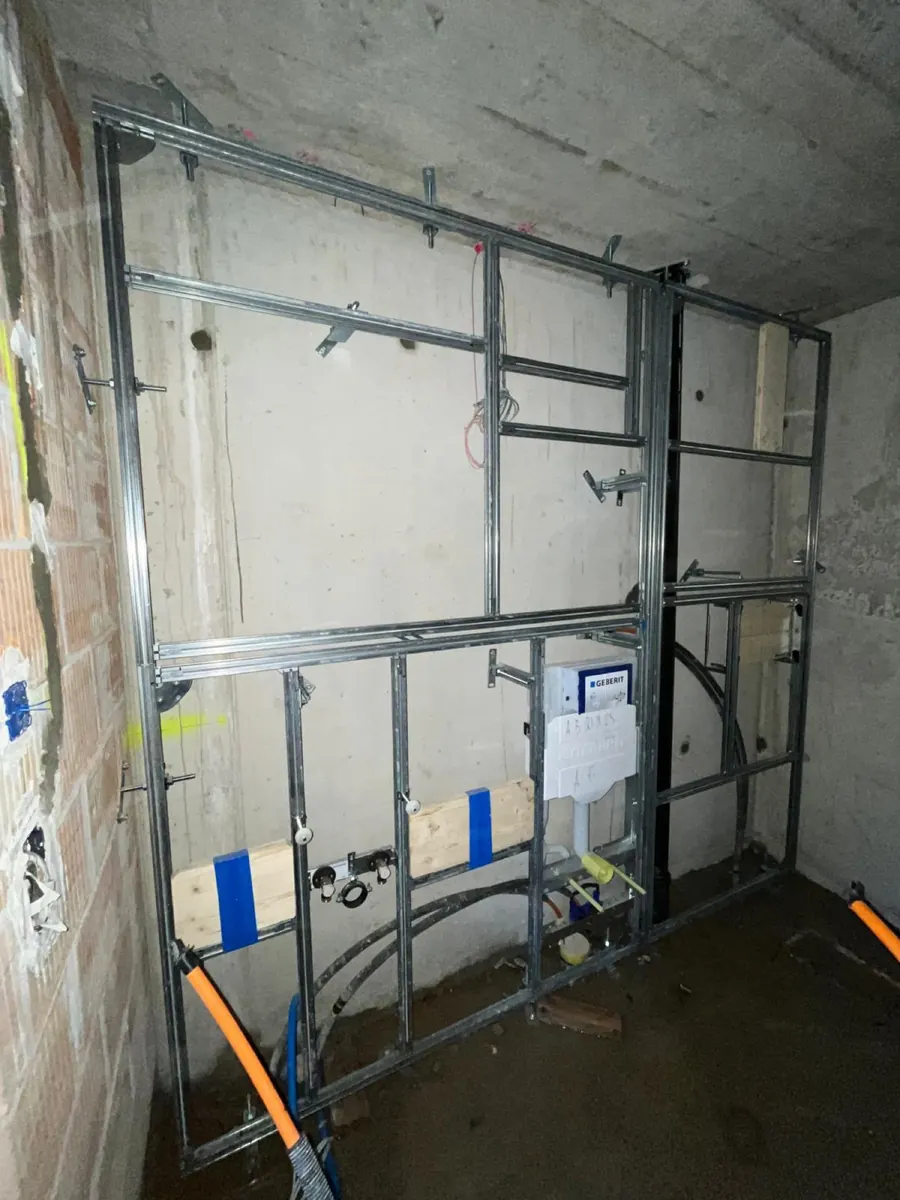 Beton bir duvarın önünde WC elemanı ve su bağlantıları olan Geberit GIS ön duvarı